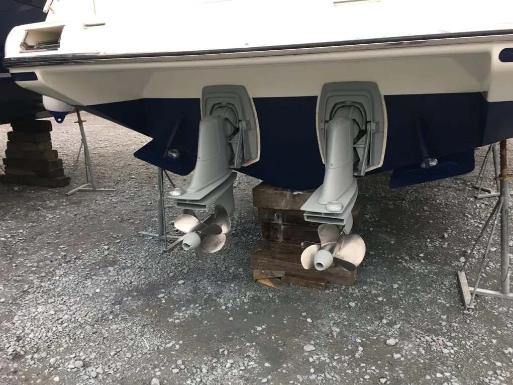 Two boat outboard motors with props are mounted at the stern, resting on supports above gravel ground.
